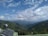 A vast mountainous landscape with lush green hills under a sky filled with scattered clouds. Solar panels and a satellite dish are installed on a structure in the foreground, overlooking the expansive view.