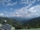 A vast mountainous landscape with lush green hills under a sky filled with scattered clouds. Solar panels and a satellite dish are installed on a structure in the foreground, overlooking the expansive view.