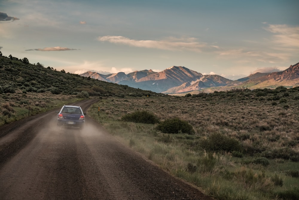 a car driving down a dirt road with mountains in the background