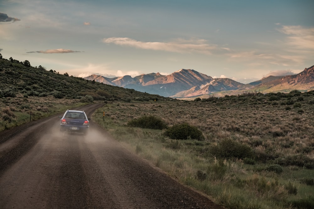 um carro dirigindo por uma estrada de terra com montanhas ao fundo