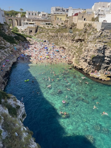 A vibrant beach scene with clear blue water and tourists relaxing under umbrellas.