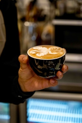 A stylish left-handed person confidently holding a coffee cup with their left hand at a café.