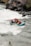 A group of four people is navigating through the rapids in a teal inflatable raft. They are all wearing safety gear, including helmets and life jackets. The river is turbulent with white water, and there are rocky cliffs and vegetation along the riverbank.