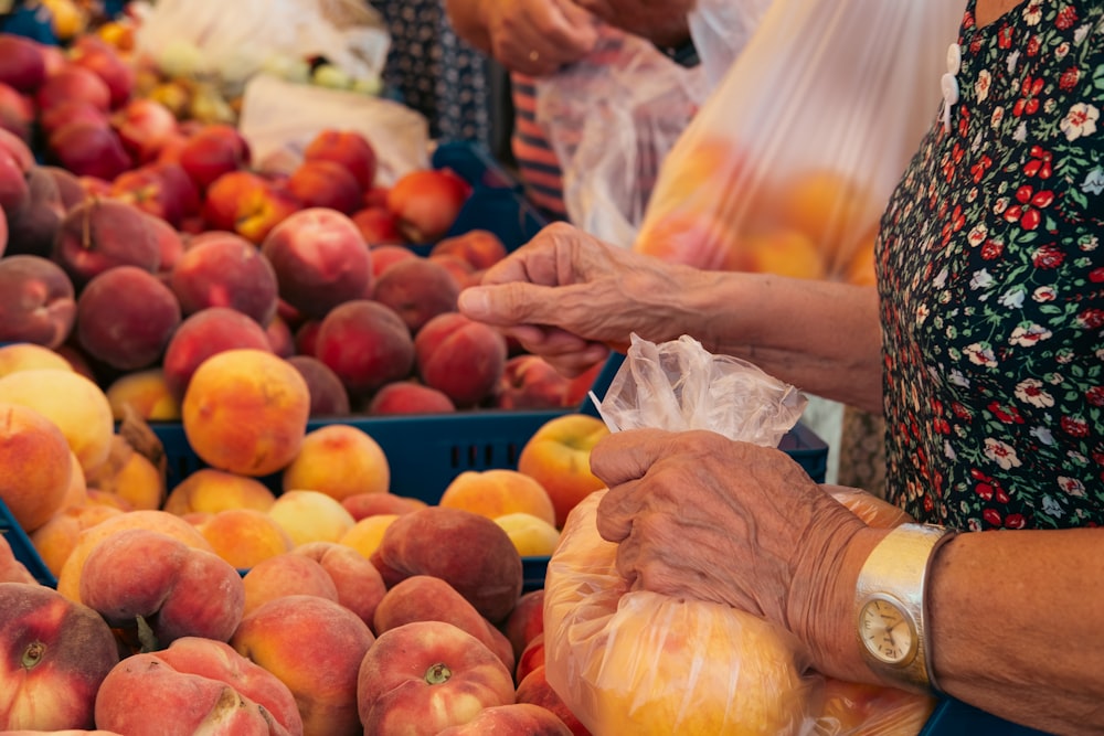 a woman holding a bag of fruit in front of a pile of peaches