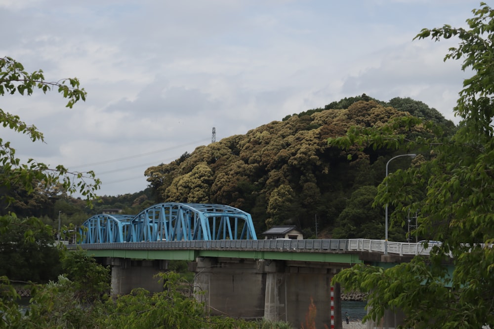 a blue bridge over a river with a mountain in the background