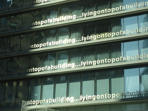 Several glass windows in a building reflecting light, with repeated text 'lyingontopofabuilding' visible across the panels.