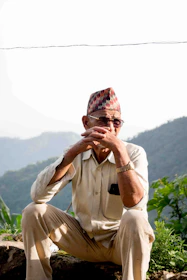 An elderly man checking his fall detection watch while gardening outdoors on a sunny day.