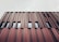 A modern building facade featuring vertical metal panels in varying shades of red and brown. The design is geometric and repetitive, with windows interspersed between the panels. The sky above is cloudy and gray, contributing to a muted overall appearance.