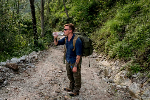 A backpacker filling a water bottle from a mountain stream surrounded by lush greenery.