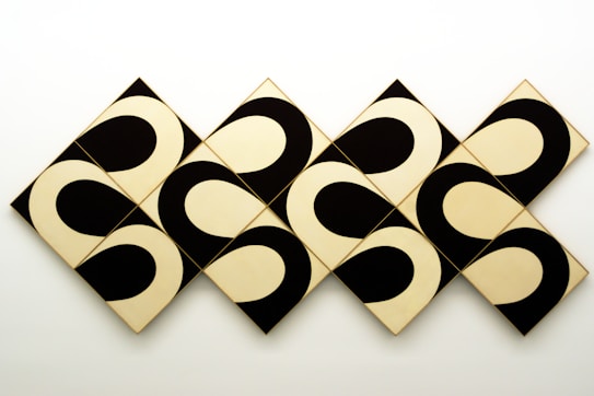 Geometric art piece featuring a series of interlocking black and white patterns on diamond-shaped tiles. The design creates an optical illusion with its repetitive curves and contrasting colors.