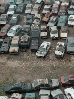 A collection of various scrap cars lined up in a recycling yard, showcasing different models and conditions.