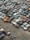 A large collection of old, rusting cars is tightly packed in an outdoor junkyard. The vehicles are in various states of disrepair, with peeling paint and visible rust. The ground around the cars is covered with dirt and scattered debris.