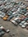A large collection of old, rusting cars is tightly packed in an outdoor junkyard. The vehicles are in various states of disrepair, with peeling paint and visible rust. The ground around the cars is covered with dirt and scattered debris.