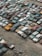 A large collection of old, rusting cars is tightly packed in an outdoor junkyard. The vehicles are in various states of disrepair, with peeling paint and visible rust. The ground around the cars is covered with dirt and scattered debris.