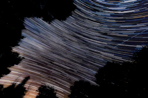 A long-exposure photo showing circular star trails over a dark forest silhouette.