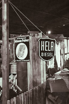 A rustic indoor setting with vintage signs, including one advertising diesel and another for a household product. There are wooden structures, a wicker basket, and assorted vintage items creating a retro atmosphere.