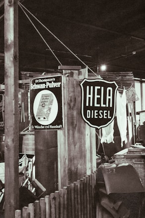 A rustic indoor setting with vintage signs, including one advertising diesel and another for a household product. There are wooden structures, a wicker basket, and assorted vintage items creating a retro atmosphere.