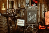 A vintage tractor with the name 'Le Robuste K40' on the front is positioned in what appears to be a rustic, possibly museum-like setting. The tractor is black with large, textured tires and has an old-fashioned steering mechanism. Several vintage posters and signs are visible in the background, enhancing the antique ambiance.