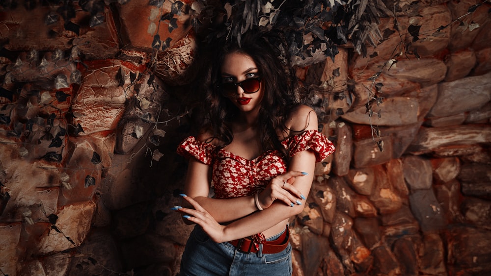 a woman wearing sunglasses leaning against a rock wall