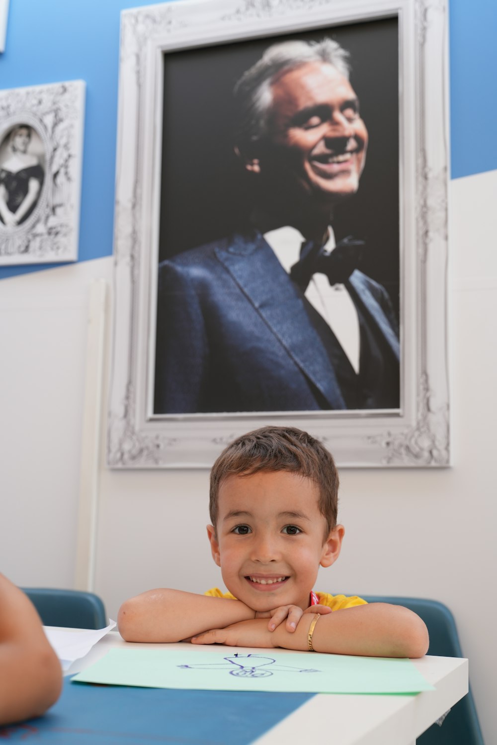 a young boy sitting at a table in front of a picture of a man