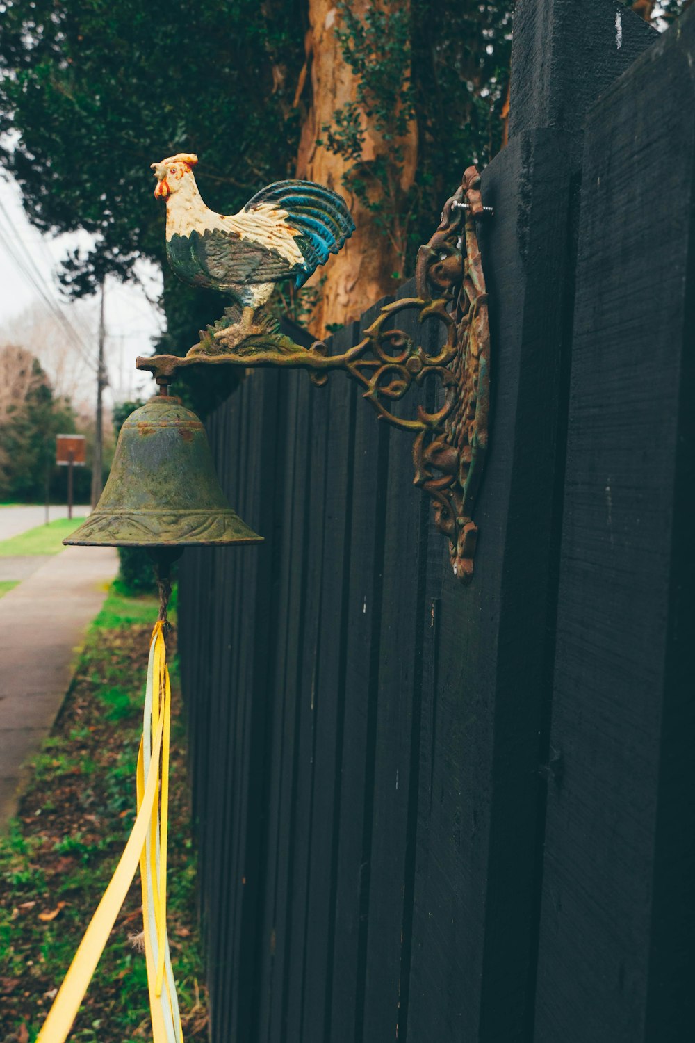 a bell with a rooster on top of it next to a fence