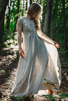 A model wearing a flowing, earth-toned dress standing in a sunlit forest clearing.