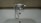 A chrome faucet is mounted on a tiled wall above a white bathtub. The faucet includes hot and cold knobs, a spout, and an attached shower head with a flexible metal hose. The wall appears to have a beige, textured surface.