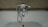 A chrome faucet is mounted on a tiled wall above a white bathtub. The faucet includes hot and cold knobs, a spout, and an attached shower head with a flexible metal hose. The wall appears to have a beige, textured surface.