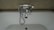 A chrome faucet is mounted on a tiled wall above a white bathtub. The faucet includes hot and cold knobs, a spout, and an attached shower head with a flexible metal hose. The wall appears to have a beige, textured surface.