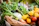A happy woman holding a basket of fresh vegetables in a sunny kitchen.