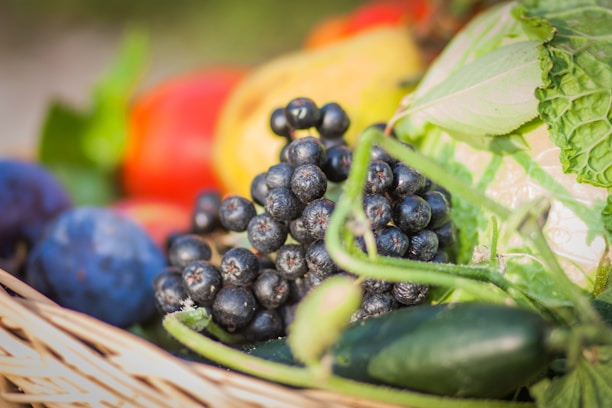 A vibrant display of fresh fruits and vegetables arranged in a rustic basket with green leaves around.