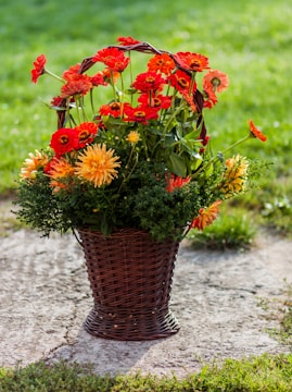A rustic basket overflowing with bright sunflowers, orange zinnias, and deep red dahlias against a backdrop of green foliage.