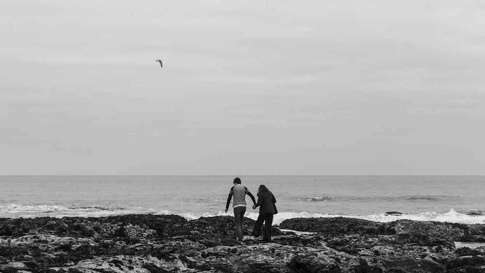 a couple of people standing on top of a rocky beach