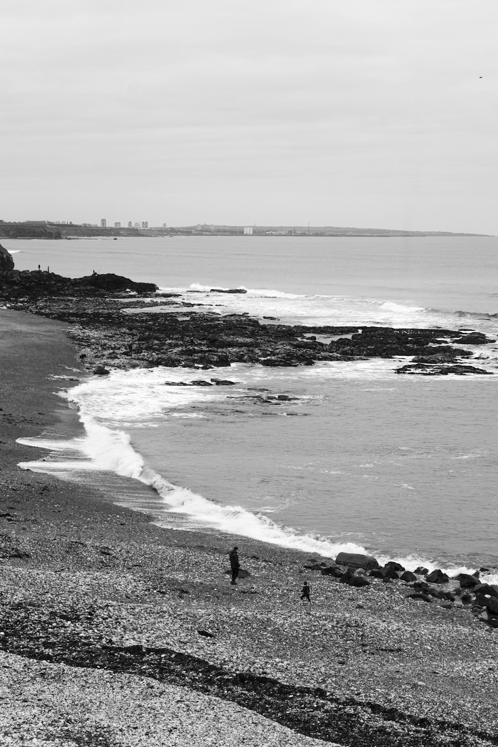 a black and white photo of people walking on the beach