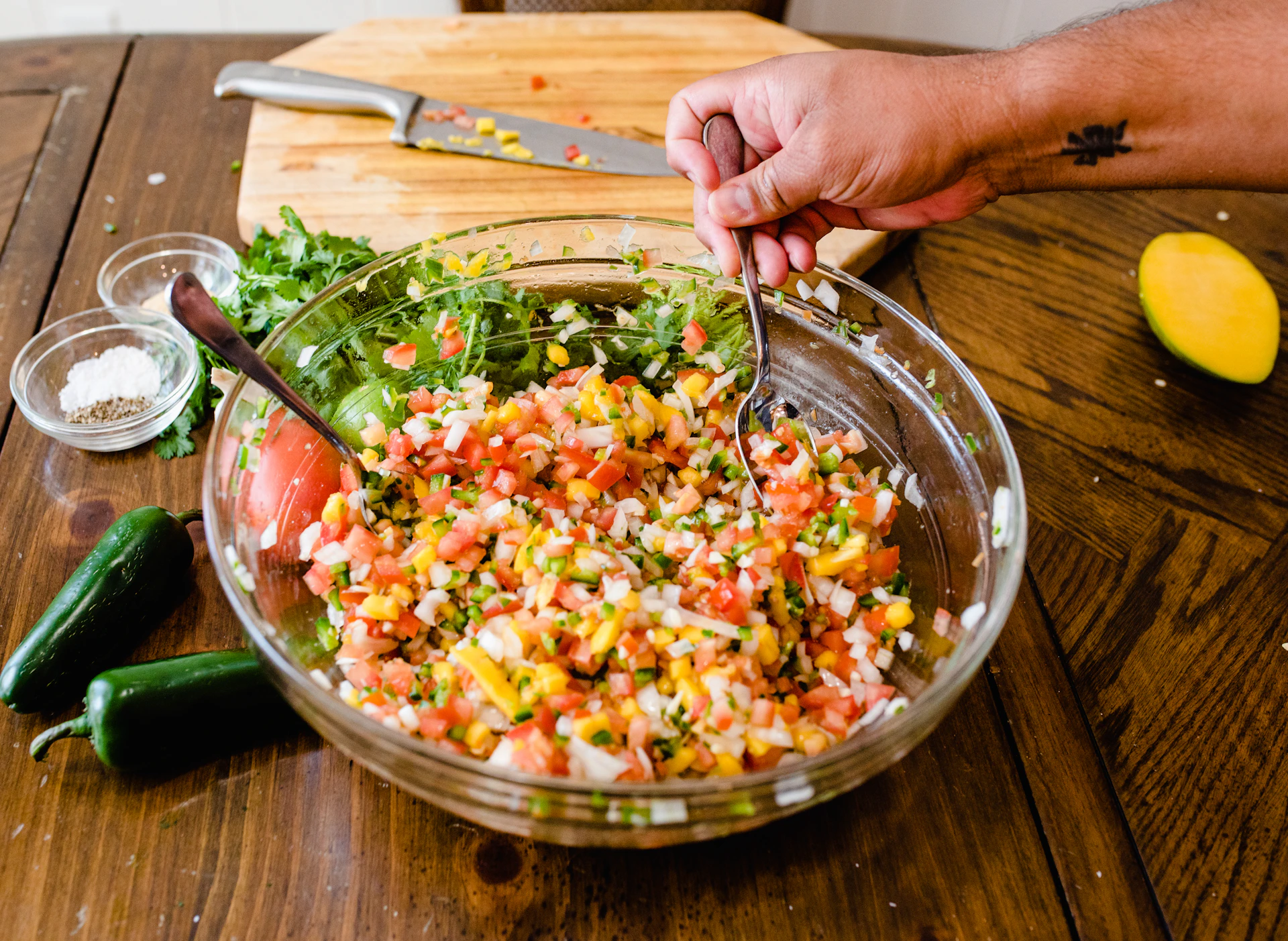 Hands stirring a bubbling pot of homemade salsa macha with vibrant red chilies and toasted sesame seeds visible.