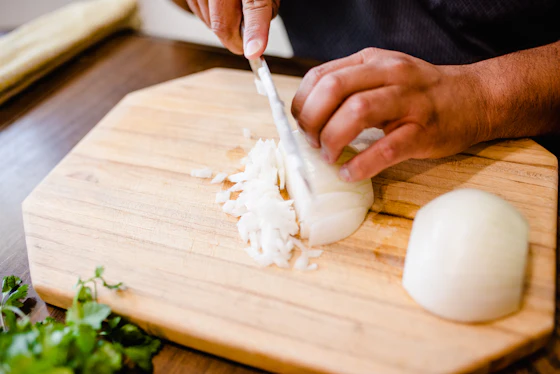 Hands chopping fresh onion on a wooden board