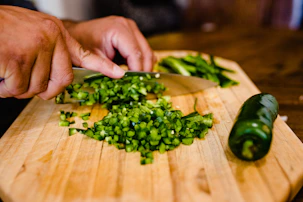 Close-up of hands chopping vegetables on a wooden cutting board in a bright kitchen.