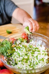 A person squeezing fresh lemon juice into a salad dressing bowl.