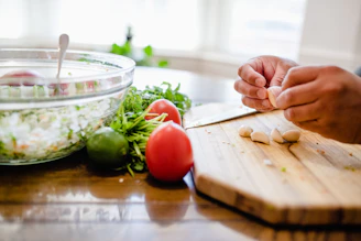 Hands preparing sambal with fresh chilies, garlic, and lime on a rustic wooden board