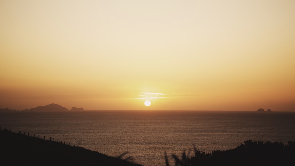 the sun is setting over the ocean with mountains in the background