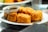 A plate of golden-brown fried tofu served with a small bowl of dark soy sauce on the side. The tofu pieces are crispy and appear appetizing, arranged neatly on a white plate.