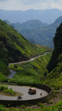 A scenic road winding through lush greenery with a motorbike and car ready for adventure.