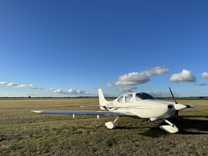 A vintage propeller plane parked on a grassy airfield under a clear blue sky.