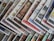 An array of colorful magazines or newspapers is spread out. Each publication features vibrant and varied cover designs, with a mix of illustrations, text, and patterns. The arrangement creates a visually dynamic and layered appearance.