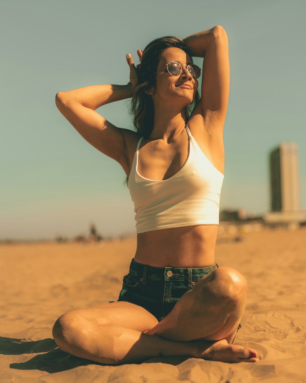 Une femme assise dans le sable avec ses mains derrière la tête