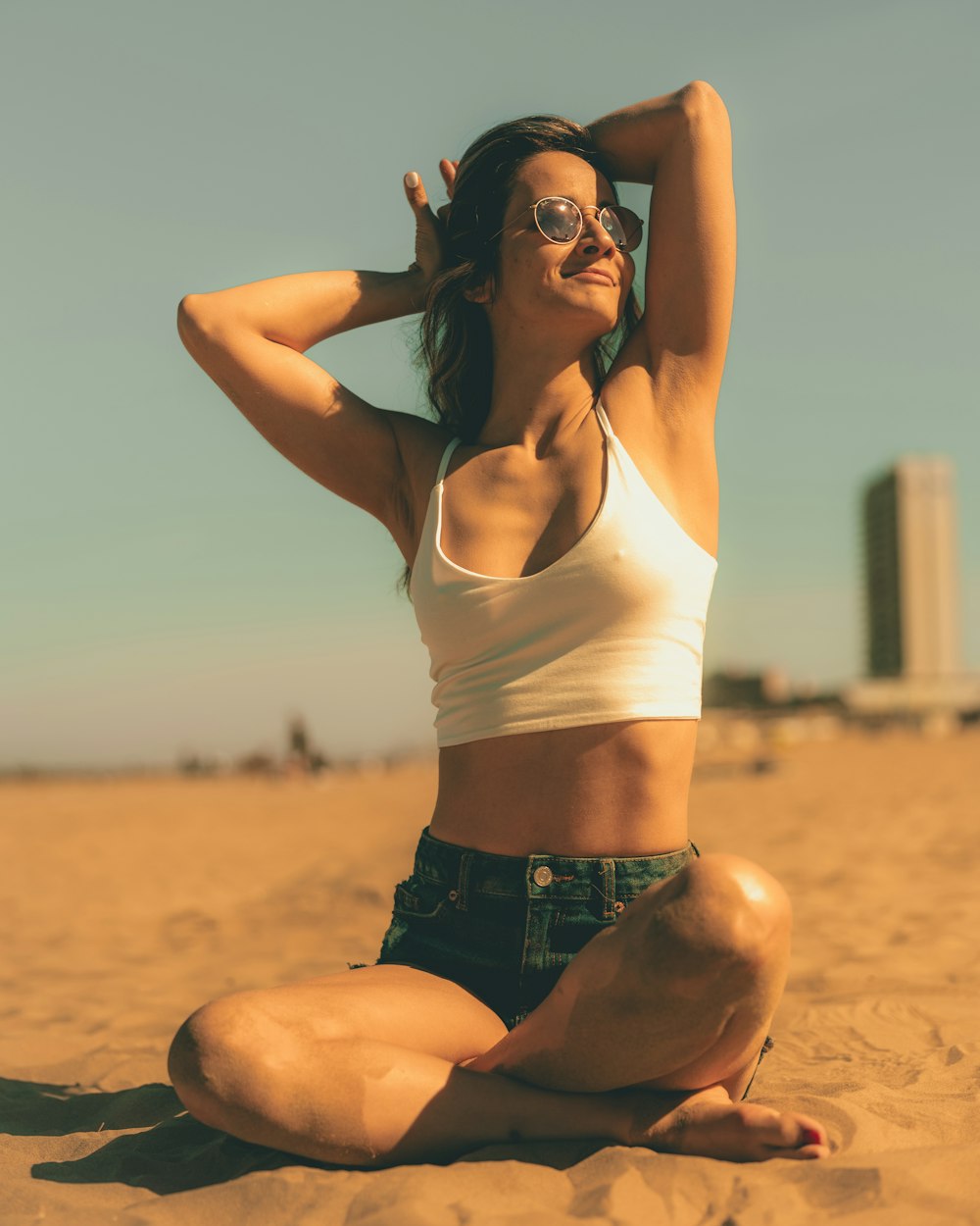 a woman sitting in the sand with her hands behind her head