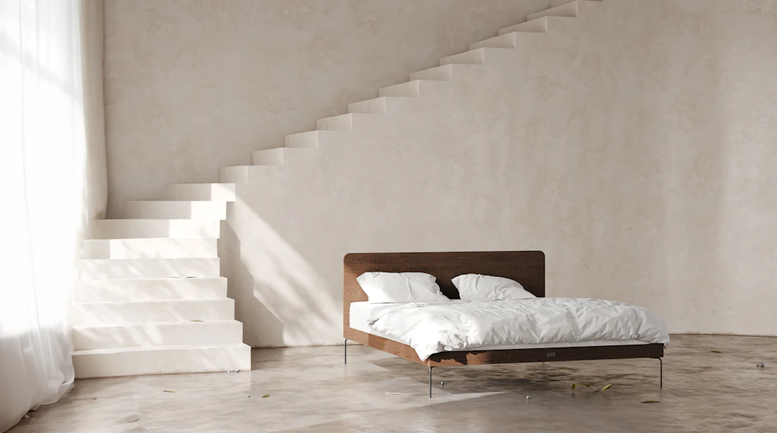 Bett mit Kopfteil aus dunklem Nussbaum unter einer hell verputzten Treppe