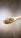 A wooden spoon filled with hemp seeds is suspended against a neutral, softly blurred background. The seeds have a pale green and beige hue and a small, round shape.