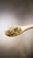 A wooden spoon filled with hemp seeds is suspended against a neutral, softly blurred background. The seeds have a pale green and beige hue and a small, round shape.