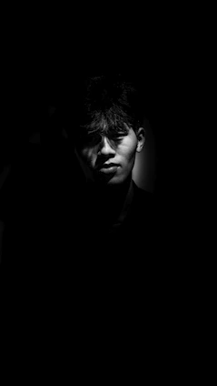 A stark black-and-white editorial portrait with dramatic shadows and generous negative space.